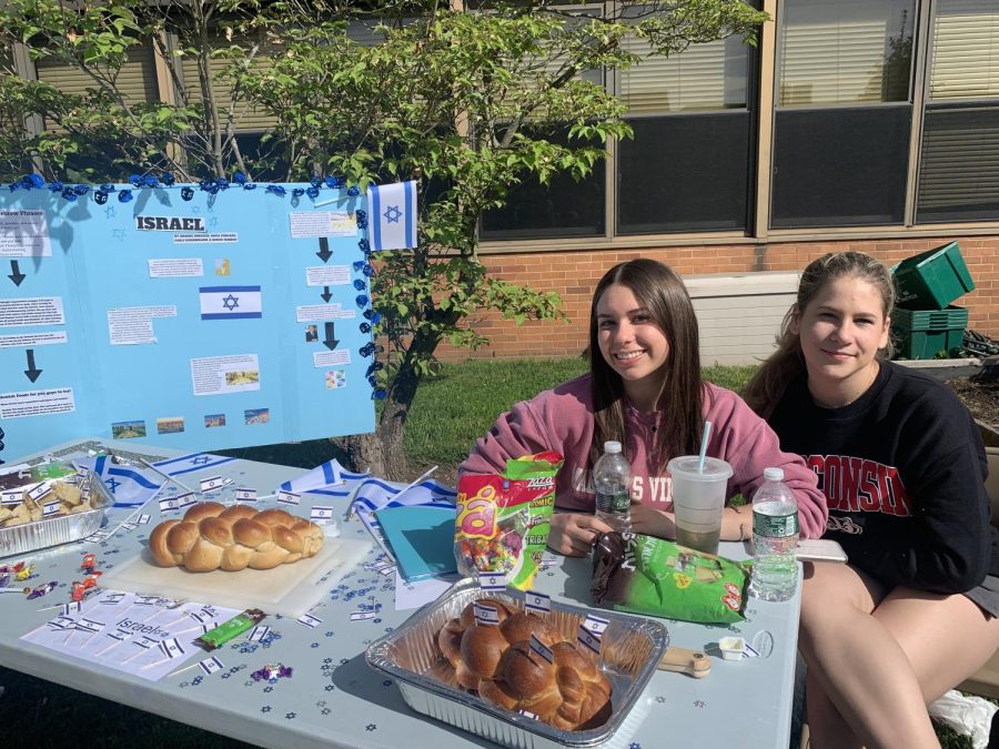 Brooke Drucker and Sofia Ferraro sit at their Israel booth with challah bread, Israeli flags, and traditional candies. 